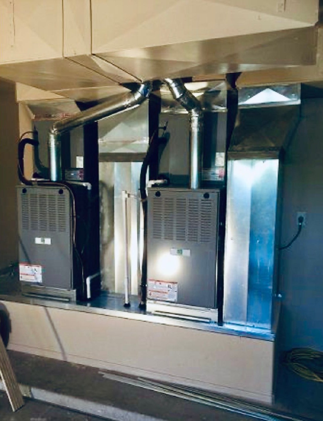 Two furnaces installed side by side with ductwork overhead
