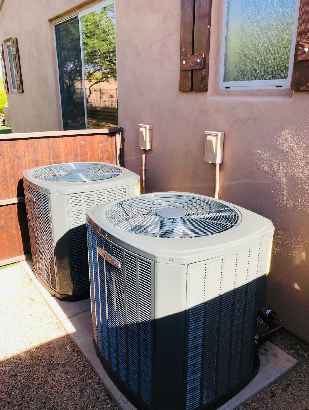 Two new condensers installed on a pad beside a stucco home