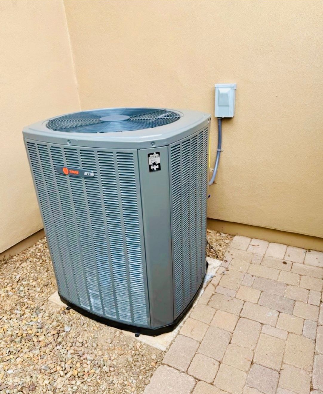 A new Trane XR condenser on a pad beside a stucco wall