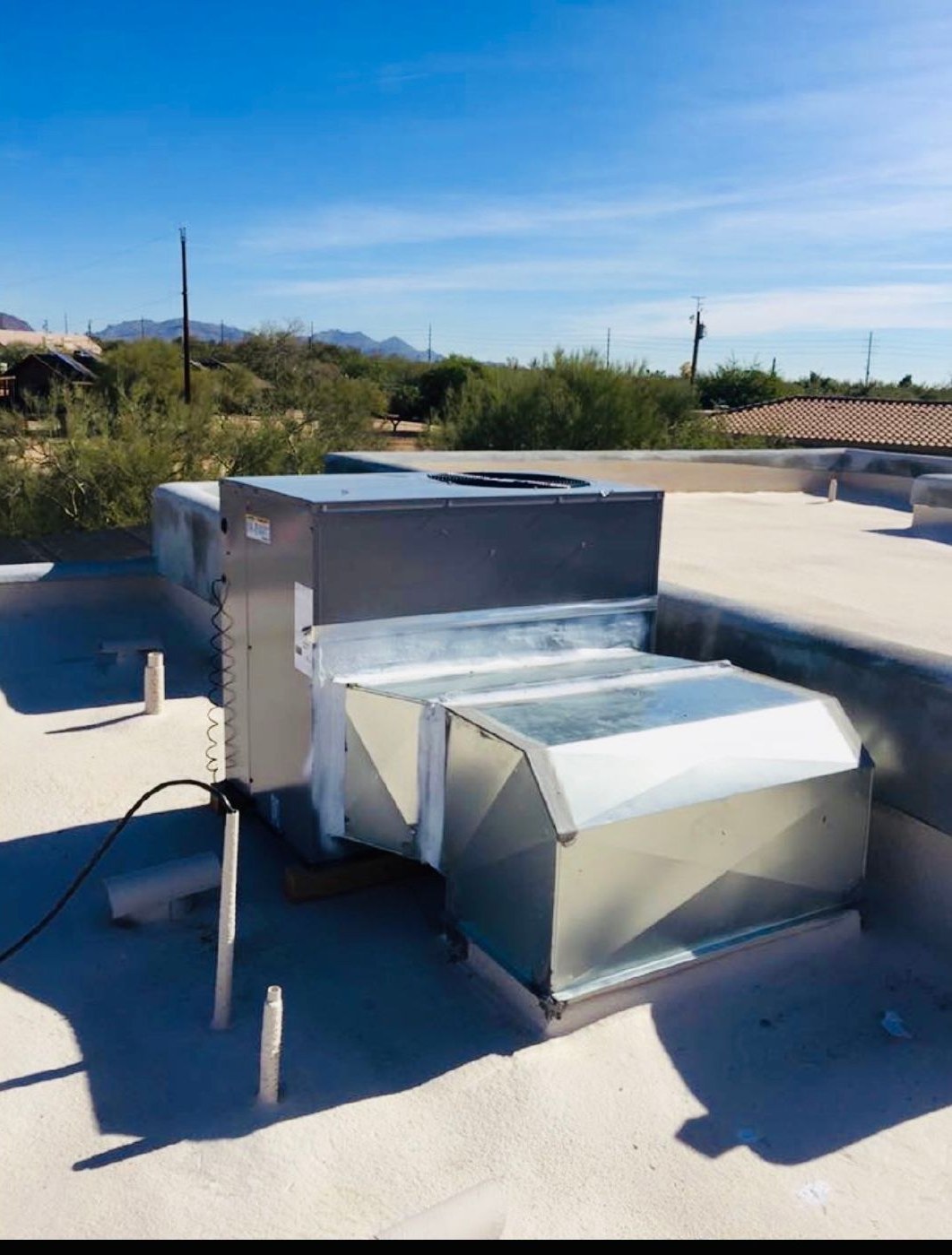 Package unit and ductwork on a flat desert roof with mountains behind